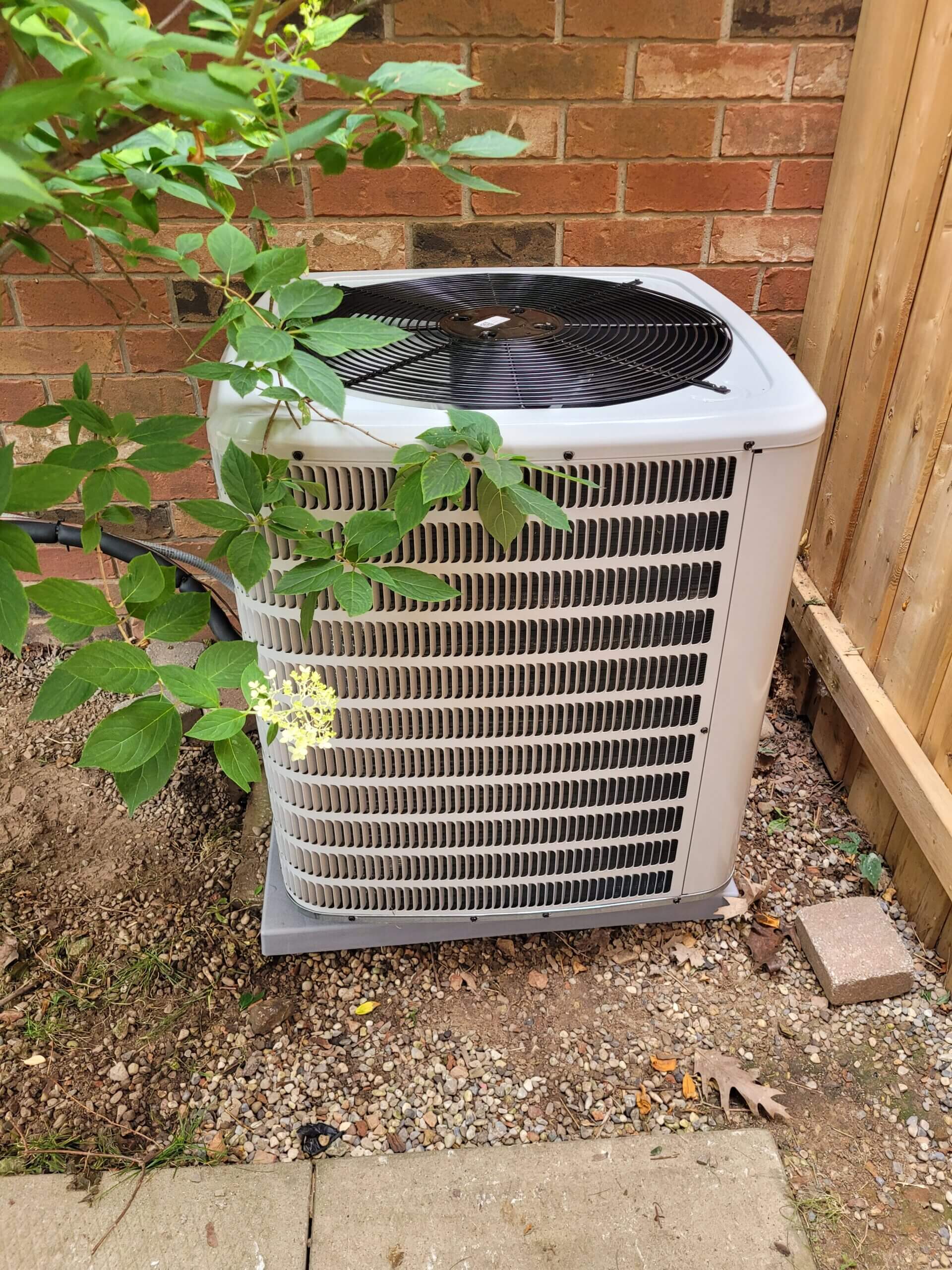 Outdoor air conditioning unit beside brick wall.