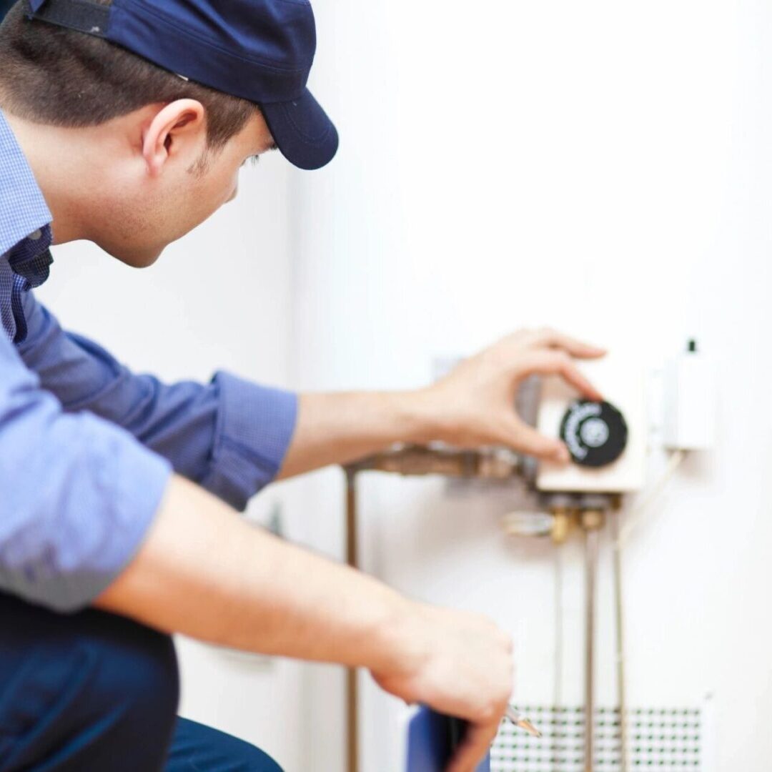 A man is fixing the water heater on the wall.